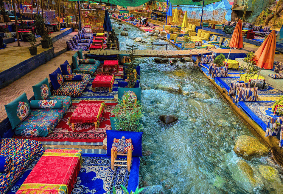 From Marrakech to Ourika Valley tour with colourful Moroccan riverside cushions, rugs, umbrellas and flowing stream