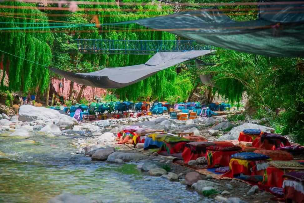 From Marrakech to Ourika Valley tour showing a rocky river lined with colourful Moroccan rugs and shaded riverside seating