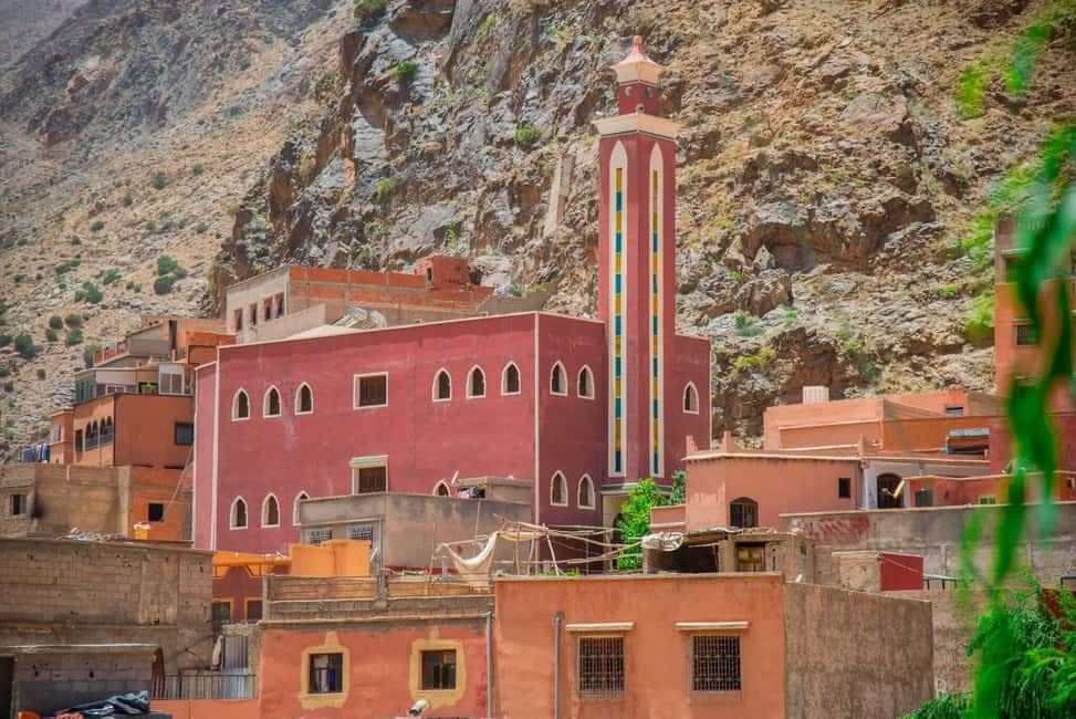 From Marrakech to Ourika Valley tour featuring a red Moroccan mosque with colourful minaret beneath rugged Atlas Mountain cliffs