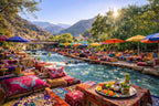 From Marrakech to Ourika Valley tour featuring a lively riverside dining area, colourful cushions, umbrellas, and mountain views