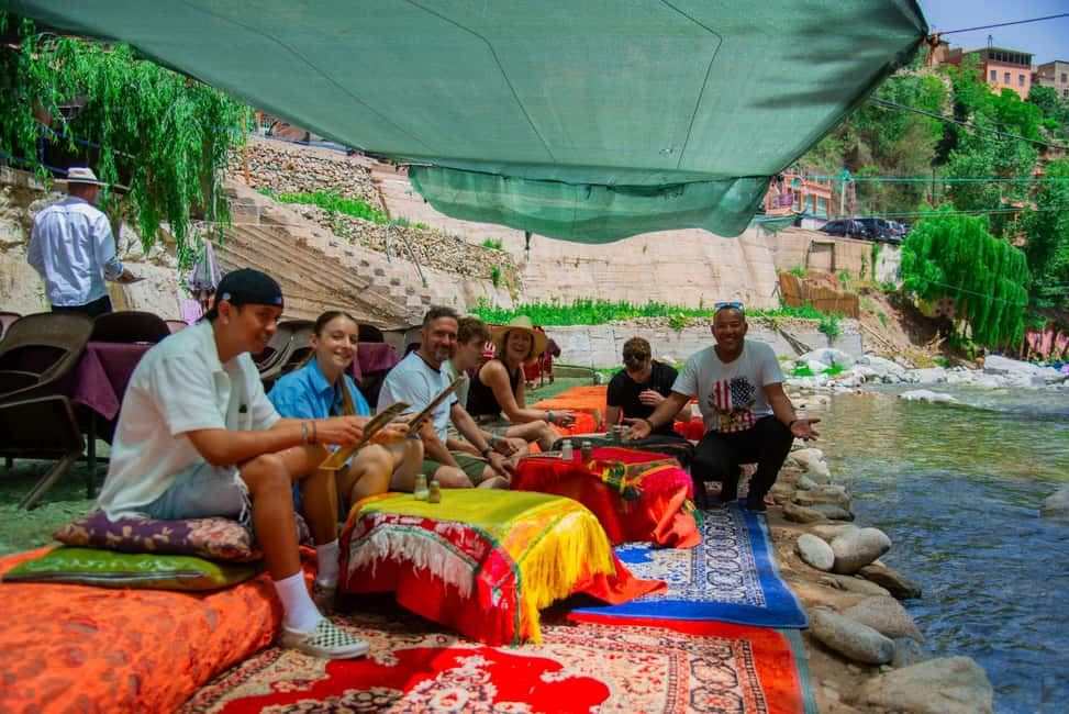 From Marrakech to Ourika Valley tour with people relaxing beside a river on colourful Moroccan rugs