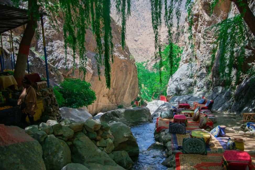 From Marrakech to Ourika Valley tour showing a rocky river gorge with lush vines and colourful riverside seating