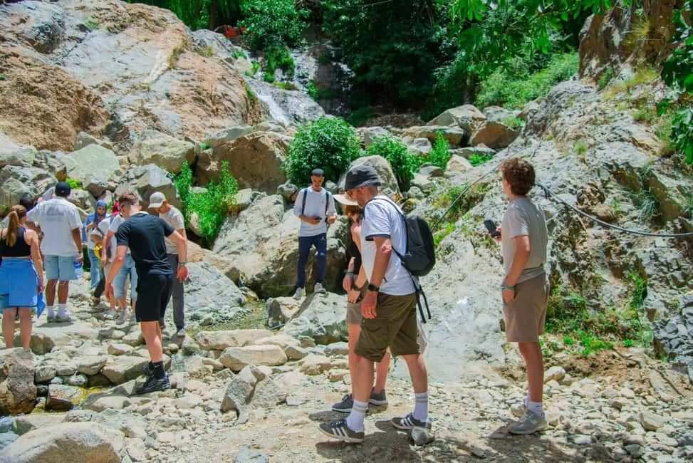From Marrakech to Ourika Valley tour hikers exploring a rocky waterfall trail with lush green foliage and cascading water