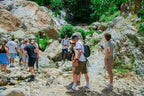 From Marrakech to Ourika Valley tour hikers exploring a rocky waterfall trail with lush green foliage and cascading water