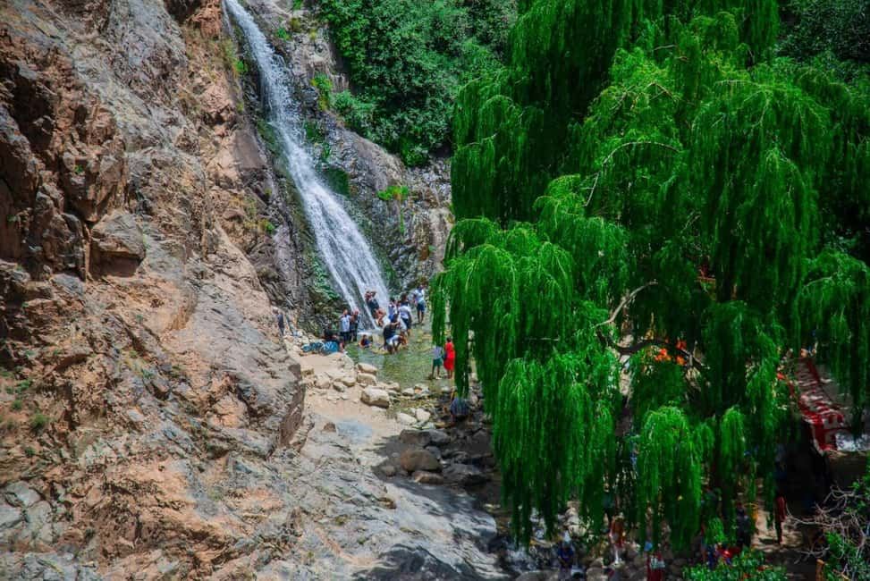 From Marrakech to Ourika Valley tour featuring a cascading waterfall, rocky cliffs, stream, and lush green trees