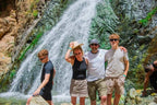From Marrakech to Ourika Valley tour group posing beside a cascading waterfall in the Atlas Mountains