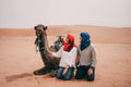From Marrakech: To Sahara Tour featuring a seated brown camel and two travellers in colourful desert clothing