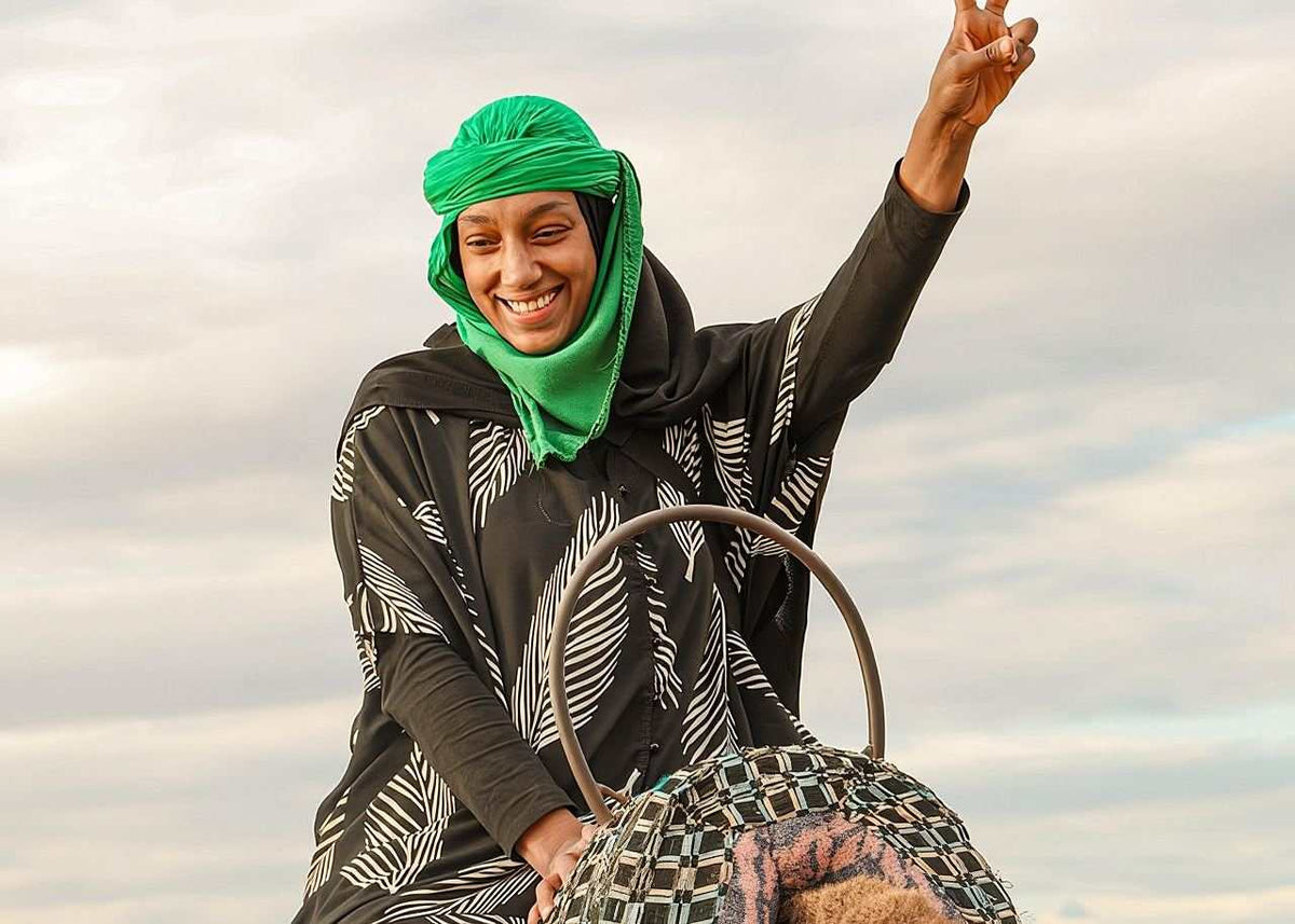 From Marrakech: To Sahara Tour featuring a smiling woman in a green headscarf and black patterned robe