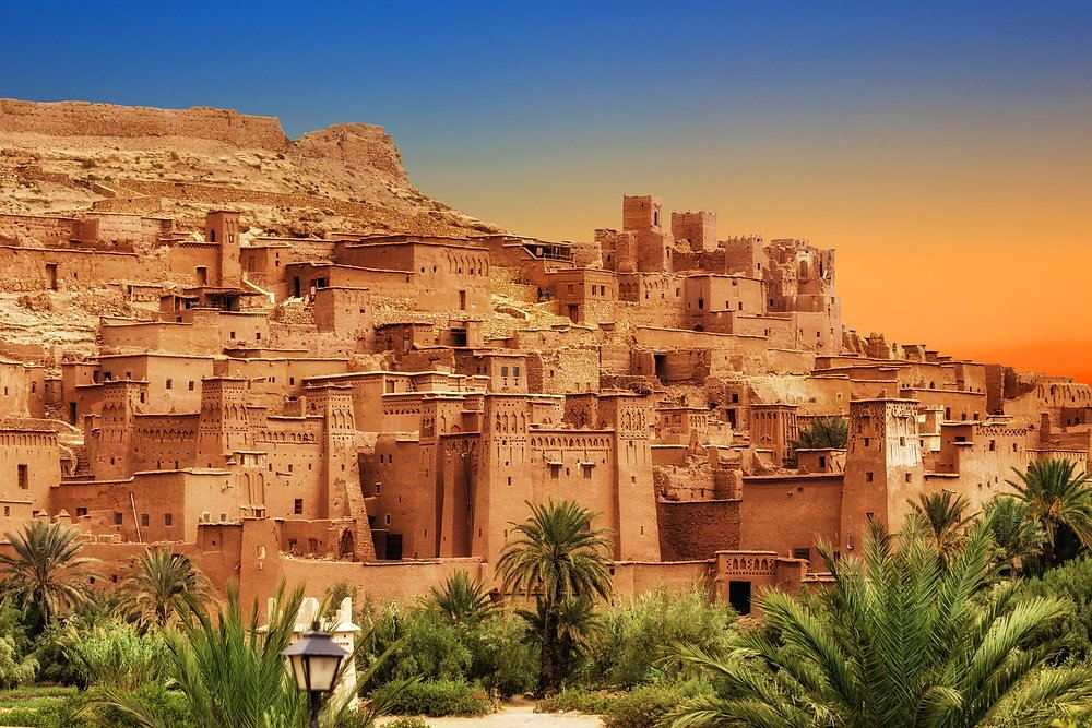 From Marrakech: To Sahara Tour featuring a warm ochre Moroccan kasbah village with palm trees and fortified towers