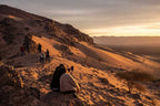 From Marrakech: To Sahara Tour showing travellers on rocky orange desert dunes beside a rugged mountain ridge
