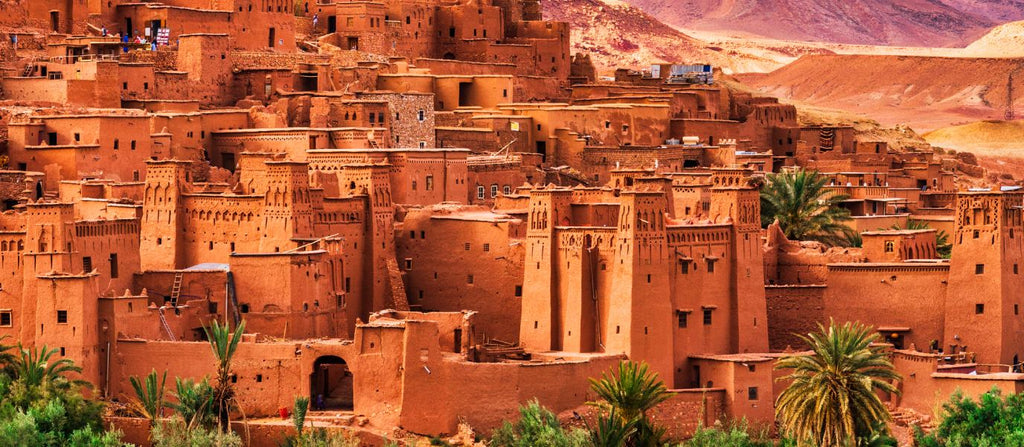 From Marrakech: To Sahara Tour featuring a historic red clay kasbah village with palms and rugged mountain terrain