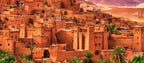 From Marrakech: To Sahara Tour featuring a historic red clay kasbah village with palms and rugged mountain terrain