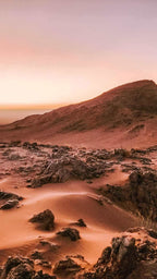 From Marrakech: To Sahara Tour showing red desert dunes with dark rocky formations beneath a pink sky