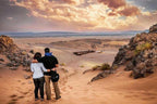 From Marrakech: To Sahara Tour showing two travelers in casual clothing overlooking a rocky sandy desert valley