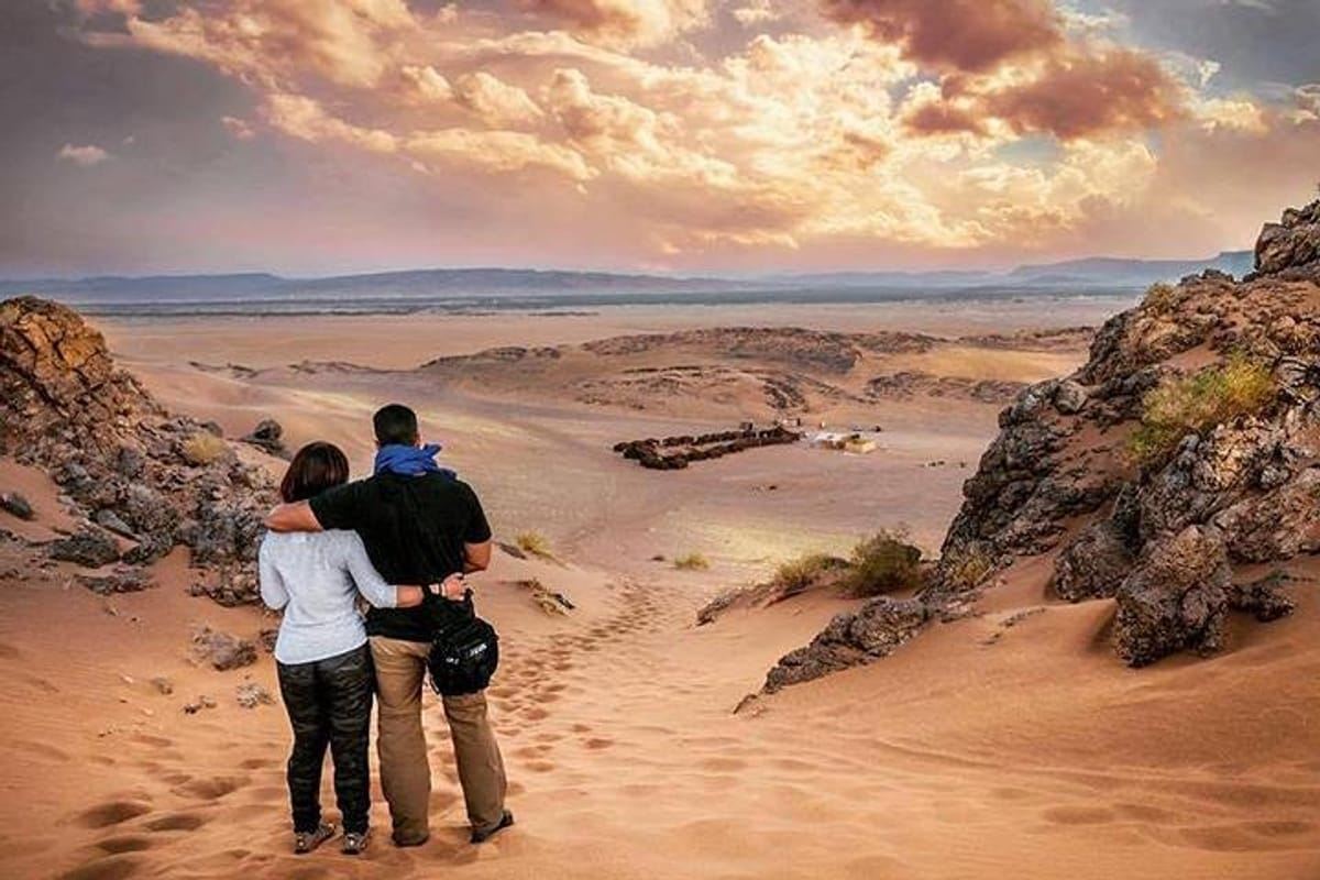 From Marrakech: To Sahara Tour showing two travelers in casual clothing overlooking a rocky sandy desert valley