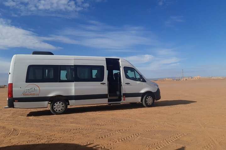 White and black passenger van with sliding door open on sandy desert terrain under blue sky for Group Tours from Marrakech.