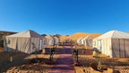 Desert camp with large beige canvas tents arranged in rows on sandy ground under clear blue sky, part of Group Tours from Marrakech.