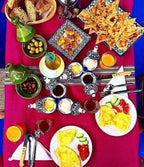 Traditional Moroccan breakfast spread with omelettes, sliced cucumbers and tomatoes, flatbread, olives, orange juice, and decorative ceramic dishes on a vibrant pink tablecloth, showcasing Group Tours from Marrakech hospitality.