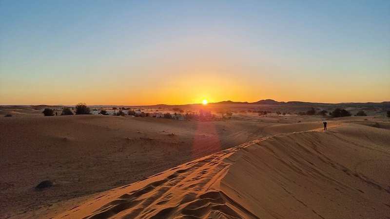 Sunset over golden sand dunes in the Sahara Desert with a distant figure walking along the ridge, perfect for Group Tours from Marrakech.