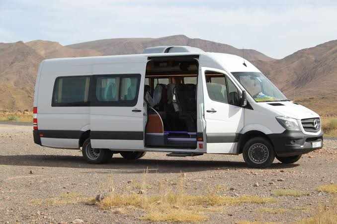 White Mercedes-Benz passenger van with sliding side door open, parked on a dry, rocky landscape for Group Tours from Marrakech.