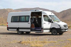 White Mercedes-Benz passenger van with sliding side door open, parked on a dry, rocky landscape for Group Tours from Marrakech.