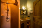 Hassilabiad Appart Hotel bathroom with warm yellow lighting, terracotta-colored built-in shower, wooden door, and decorative mirror