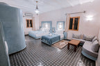 Hassilabiad Appart Hotel bedroom with two beds, blue and gray bedding, patterned tiled floor, and built-in curved seating area