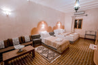 Hassilabiad Appart Hotel bedroom featuring two beige beds, Moroccan-style patterned floor tiles, sofa and decorative wall lamps