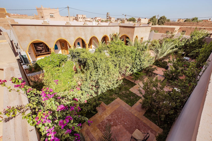 Hassilabiad Appart Hotel courtyard garden with lush greenery, flowering plants, arched windows, and beige stone walls