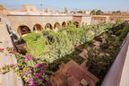Hassilabiad Appart Hotel courtyard garden with lush greenery, flowering plants, arched windows, and beige stone walls