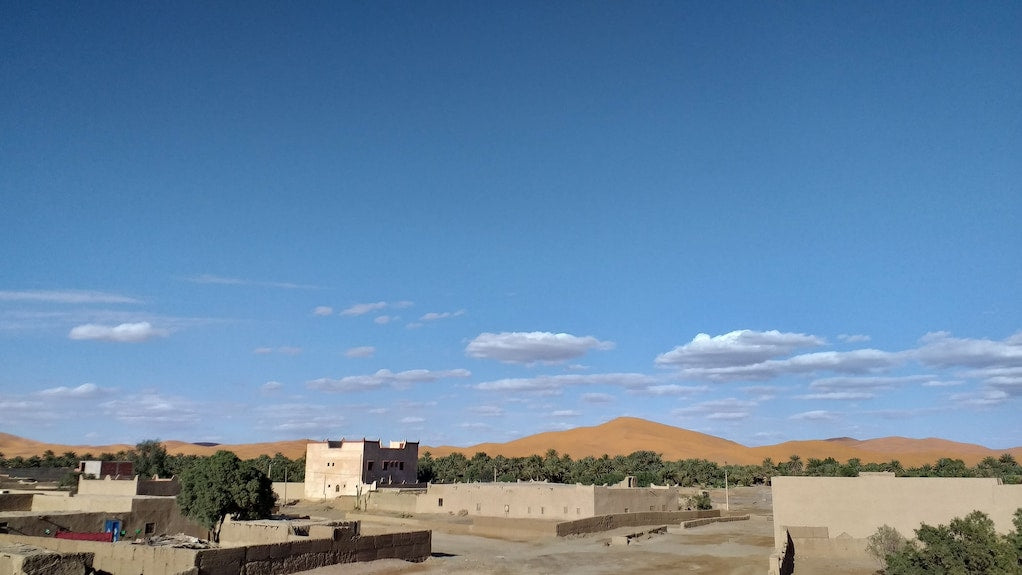 Hassilabiad Appart Hotel surrounded by desert landscape with sand dunes, clear blue sky, and sparse greenery