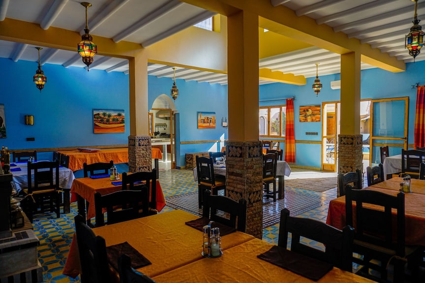 Hassilabiad Appart Hotel dining area with blue walls, tiled floors, yellow columns, dark wood chairs and orange tablecloths