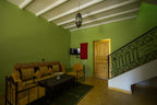 Hassilabiad Appart Hotel living room with green walls, wooden ceiling beams, wrought iron staircase, and mustard cushioned seating