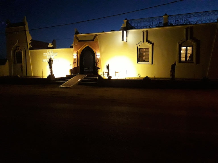 Hassilabiad Appart Hotel at night with illuminated beige exterior walls and arched entrance in Merzouga