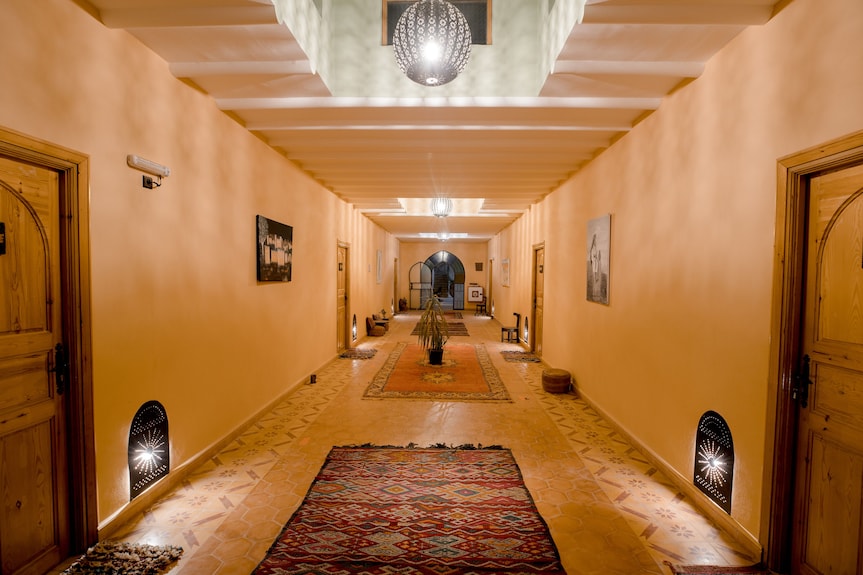 Interior corridor of Hassilabiad Appart Hotel with warm tan walls, traditional patterned rugs, wooden doors, and hanging lanterns