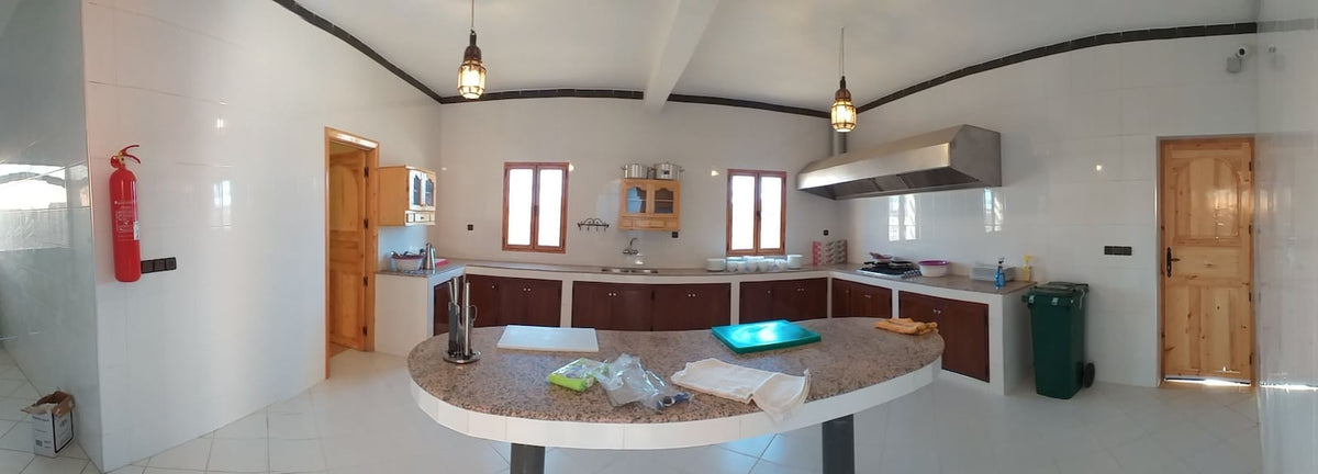 Hassilabiad Appart Hotel kitchen with white tiled walls, wooden cabinets, granite island countertop, and stainless steel range hood