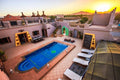 Outdoor swimming pool at Hassilabiad Appart Hotel with blue water, surrounded by sun loungers and tan tiled patio at sunset
