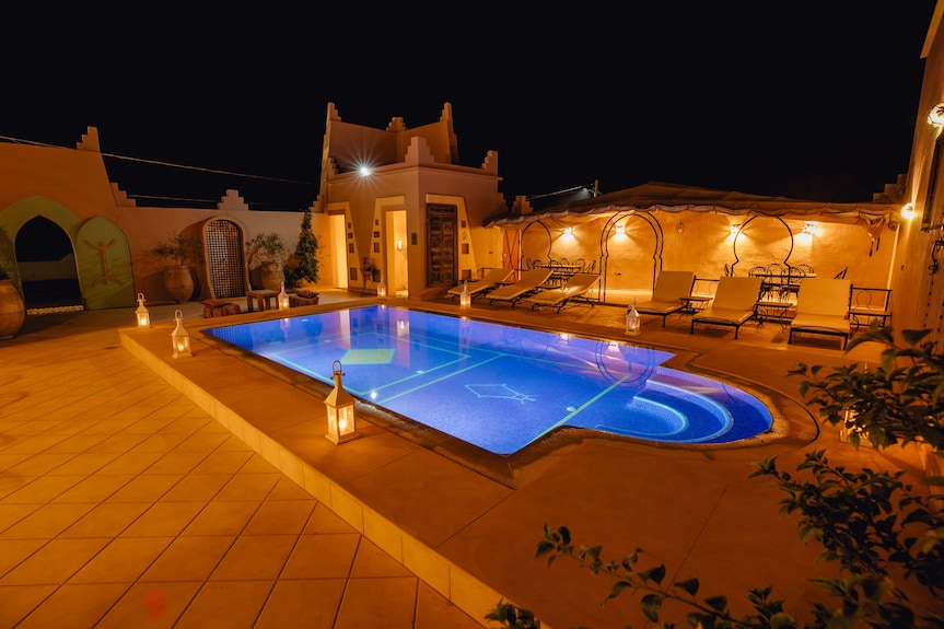 Hassilabiad Appart Hotel outdoor swimming pool illuminated at night with surrounding sun loungers and warm wall lighting