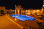 Hassilabiad Appart Hotel outdoor swimming pool illuminated at night with surrounding sun loungers and warm wall lighting