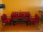Lounge area with red cushioned iron frame sofa and chairs, wooden coffee table, orange walls and carpet at Hassilabiad Appart Hotel