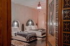 Hassilabiad Appart Hotel room with two beds, white bedding, grey striped blankets, Moroccan-style decor, and a wooden door with intricate patterns