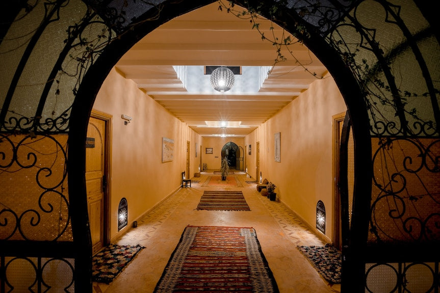 Hassilabiad Appart Hotel hallway with warm orange walls, patterned rugs, decorative iron archway, and ceiling light fixtures