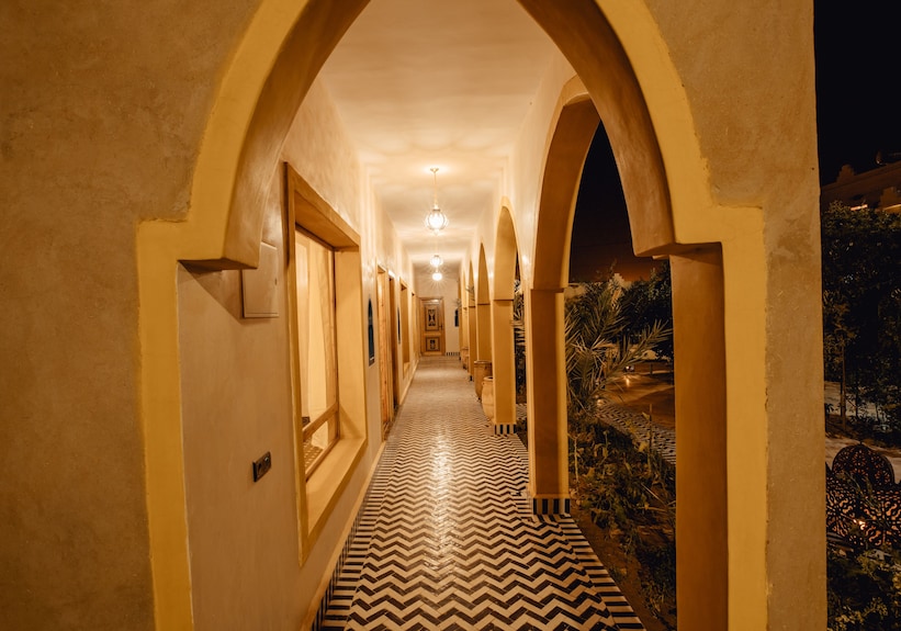 Hassilabiad Appart Hotel corridor with yellow arched walls and zigzag patterned floor tiles under warm lighting at night