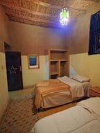 Hostel Dar Lgamra bedroom with beige walls, two single beds, wooden ceiling, patterned rug, and colorful hanging light