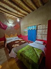 Hostel Dar Lgamra cozy room with twin beds, traditional Moroccan textiles, wooden ceiling beams, and vibrant colored blankets