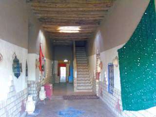 Hostel Dar Lgamra interior hallway with rustic wooden ceiling, traditional decor, patterned carpets, and stairs in Merzouga