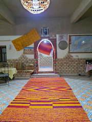Hostel Dar Lgamra interior with vibrant patterned orange, red, and purple carpet leading to arched doorway and traditional decor elements.