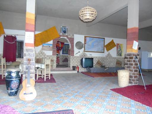 Hostel Dar Lgamra interior with tiled floor, traditional cushions, hanging woven light, musical instruments, and brick pillars
