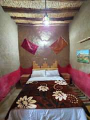 Hostel Dar Lgamra rustic bedroom with wooden ceiling, earth-toned walls, patterned bedspread, and colorful wall hangings