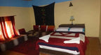 Hotel auberge Sahara room with double bed featuring red and white bedding, corner seating with cushions, and tasseled curtains